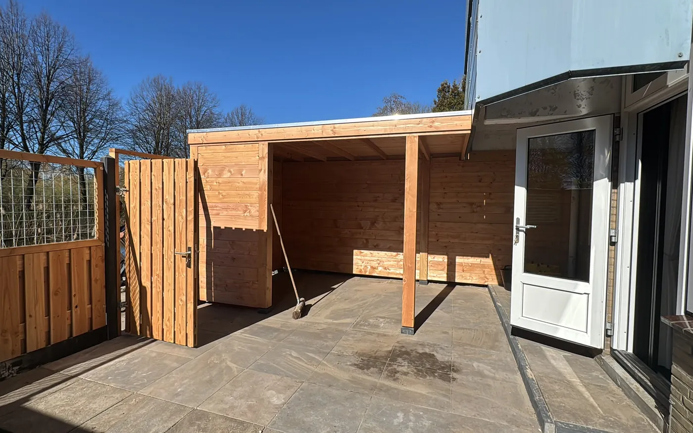 Houten berging met overstek en aansluitende schutting in de tuin