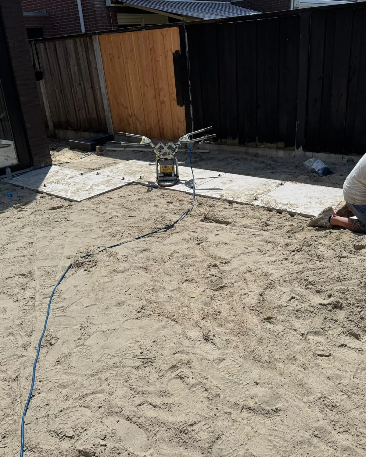 Vakman van S&B Bouw en Tuin stelt een tegel op het zandbed tijdens de aanleg