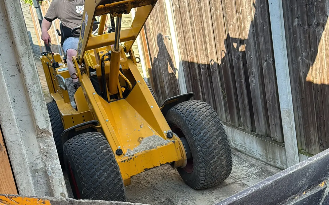 Een shovel voert grond af door de smalle doorgang naast de woning